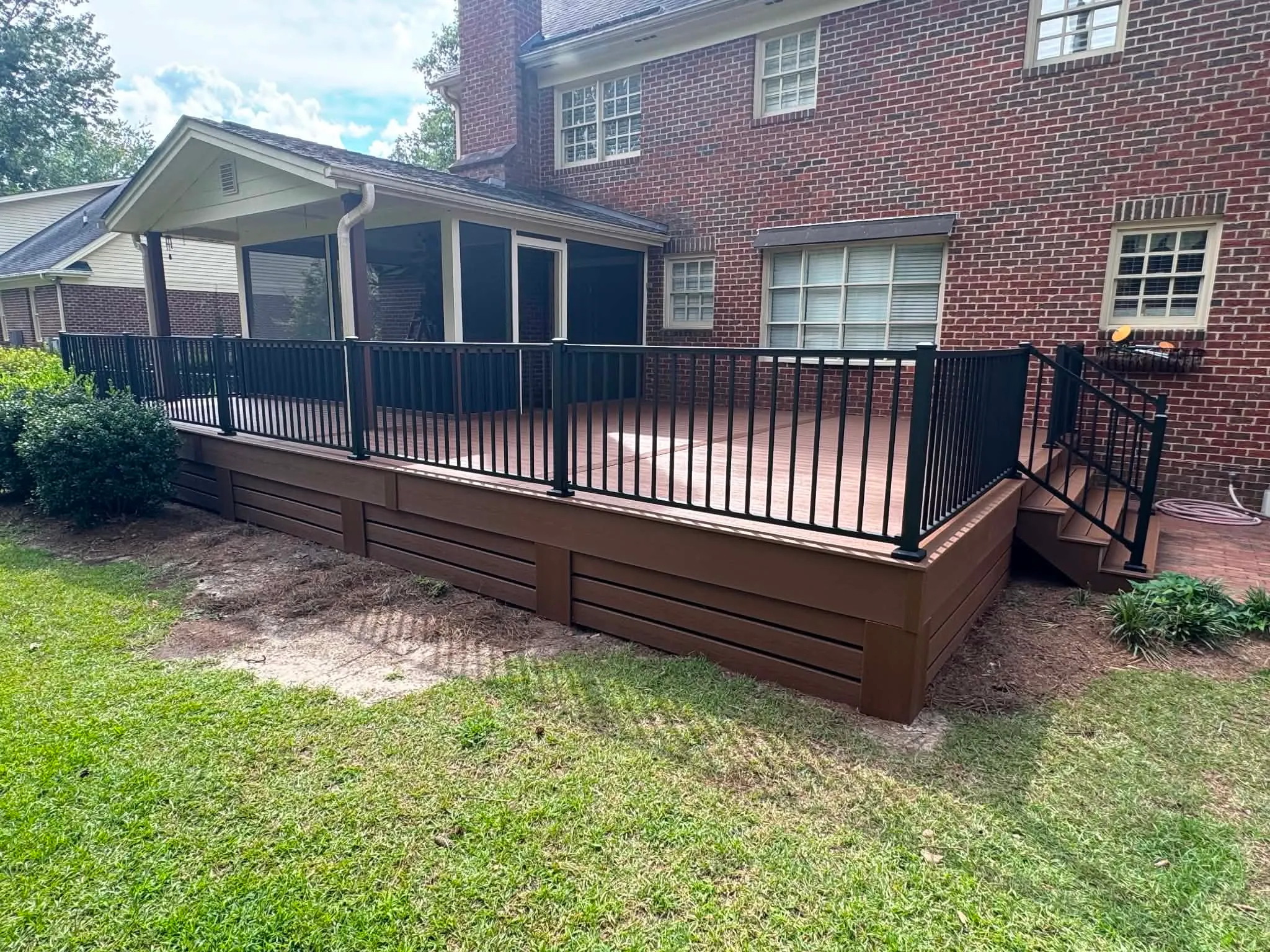Rebuilt outdoor deck and screened porch beside a brick home